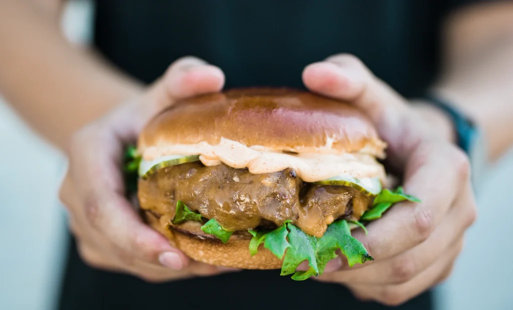 Burger med oksekød, salat og dressing holdt i to hænder